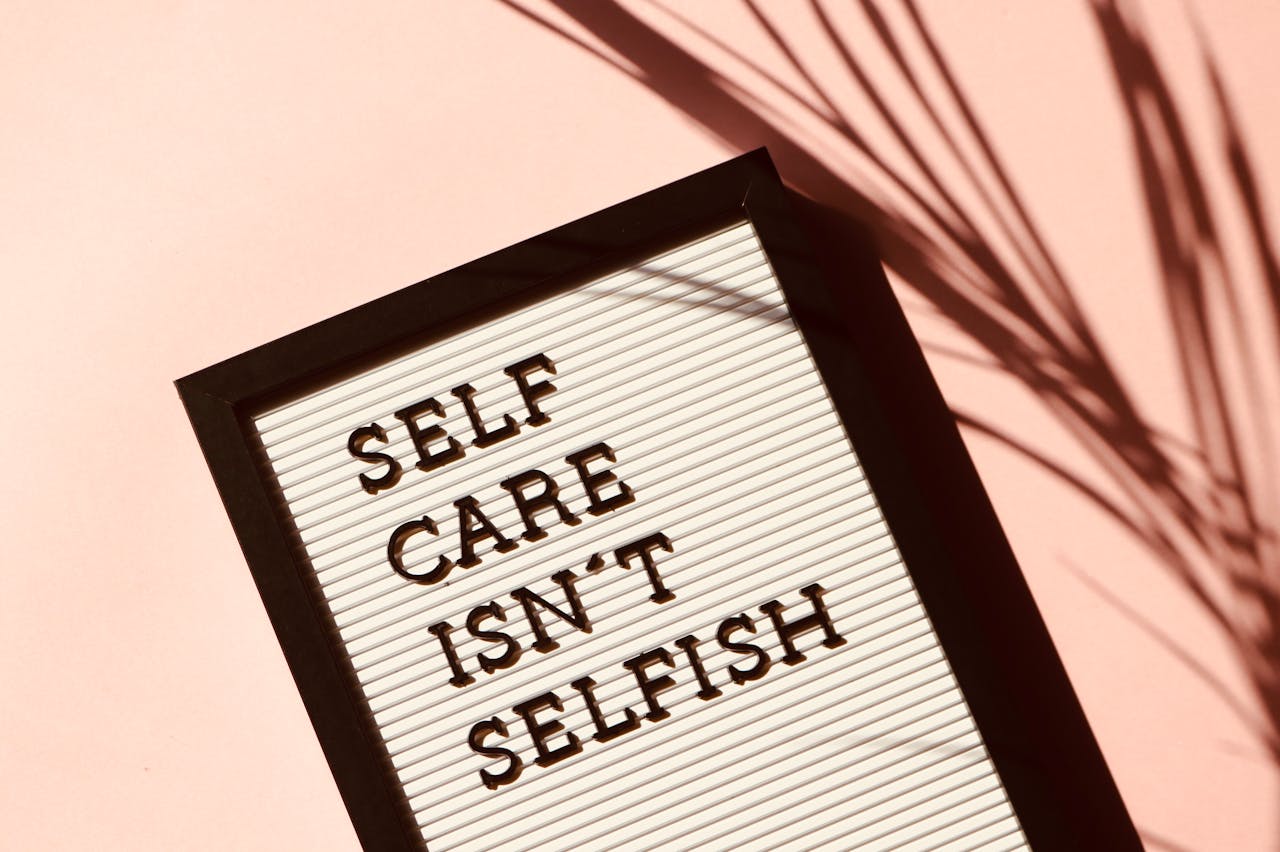 Letter board displaying Self Care Isnt Selfish with artistic shadow on pink background.